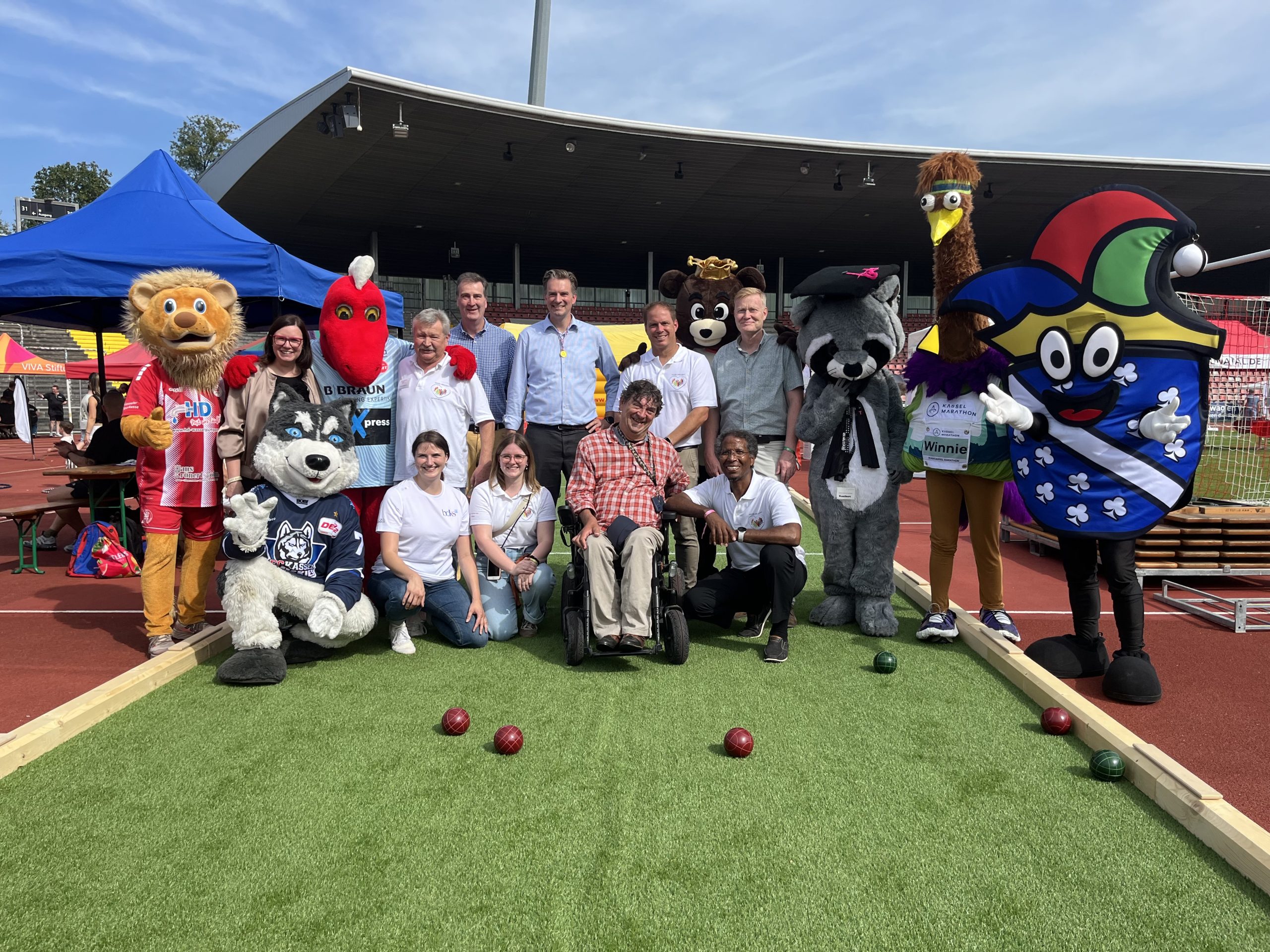 v.l.n.r.: Manuela Strube (Staatssekretärin), Michael Siegmund (Sportkreis Region Kassel e. V.), Anna-Lena Otto (bdks), Prof. Gerrit Jungk (Vorstand bdks), Kiara Dittmar (Sportamt Kassel), Sven Schoeller (Oberbürgermeister Kassel), Andreas Winkel (Landesbeauftragter für Menschen mit Behinderungen), Dr. Tobias Heyer (Sportamtsleiter), Alem Andezion (Sportamt Kassel), Heiko Lehmkuhl (Sportdezernent) zusammen mit den Maskottchen verschiedener Vereine auf der geförderten Boccia-Bahn. Foto: Sophia Landgrebe